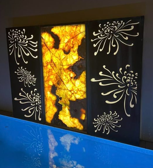 A decorative laser-cut screen lit from behind beside a pool