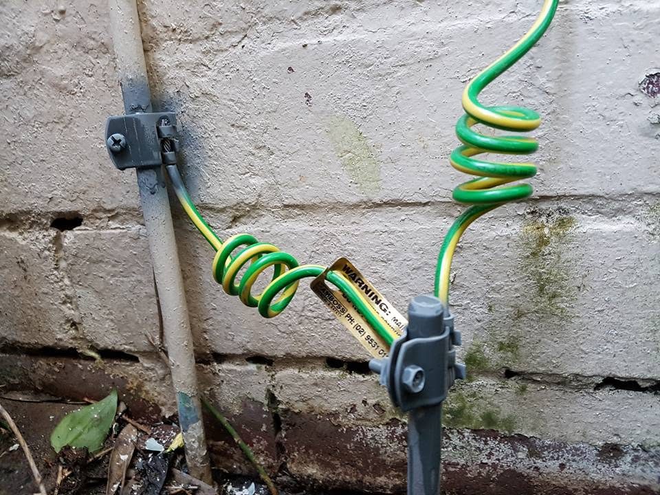 A green and yellow earthing conductor fixed along a sandstone wall