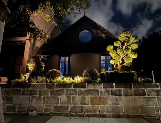 Garden and facade lighting at night above a sandstone wall
