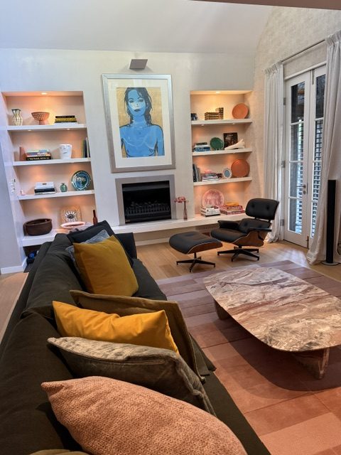 A living room with lit joinery shelves either side of a fireplace and a downlight on the artwork above it