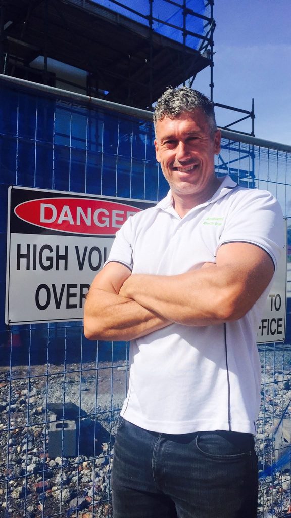Peter Stafford standing in front of a High Voltage warning sign on a work site