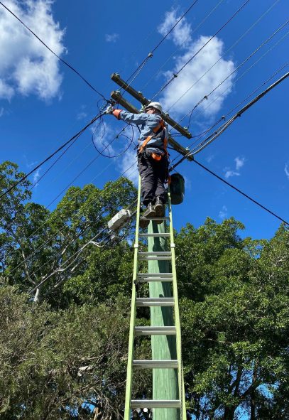 An electrician on a ladder working at overhead service mains