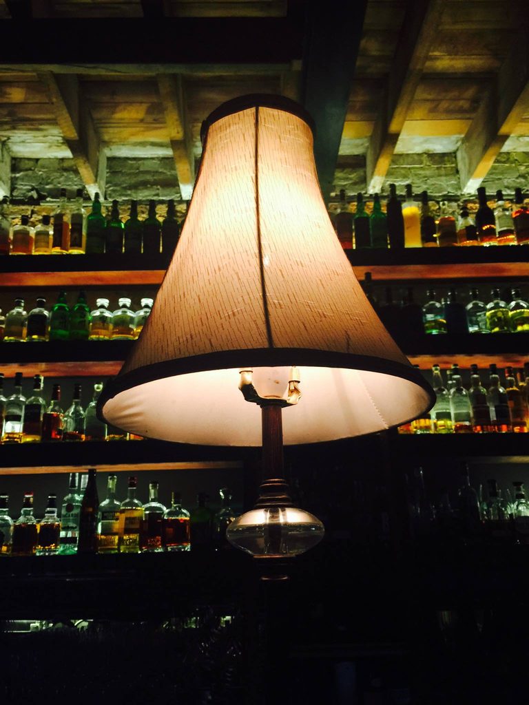 A large fabric floor lamp lit in front of a bar's back shelves