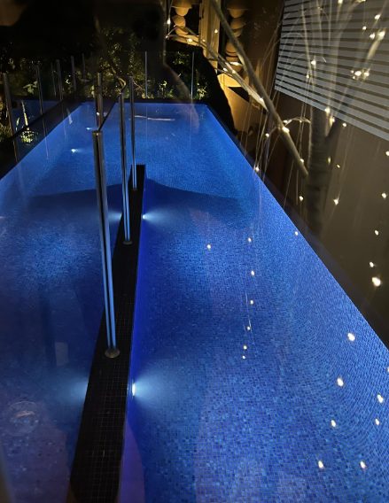 A lap pool lit from underwater at night beside a lit feature wall