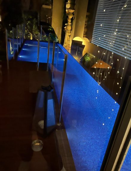 A pool lit blue at night beside a terrace strung with small lights