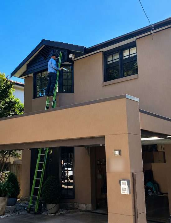 An electrician on a ladder at the service entry of a two-storey house